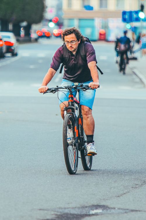 Free Man cycling on city street in Riga, showcasing urban transportation and active lifestyle. Stock Photo