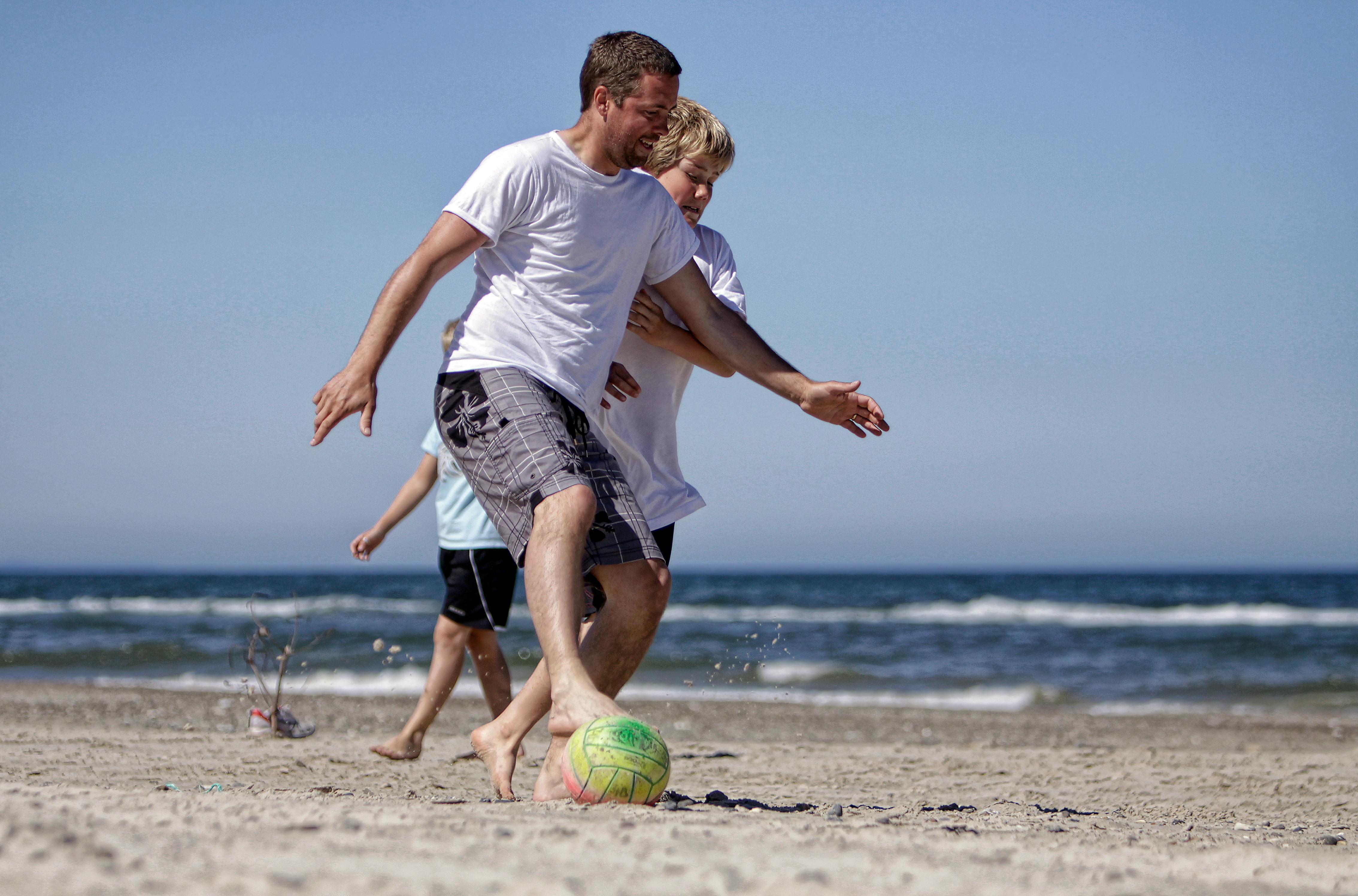 A lively game of beach football with a group of friends enjoying a sunny day by the sea.