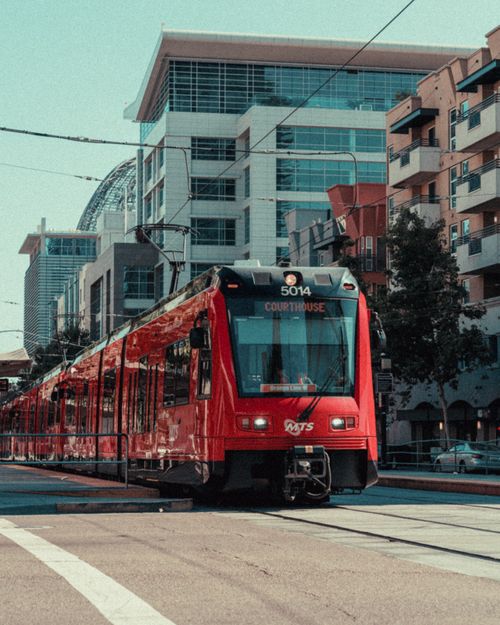 Free A vibrant red tram travels through a bustling city street, showcasing modern urban architecture. Stock Photo