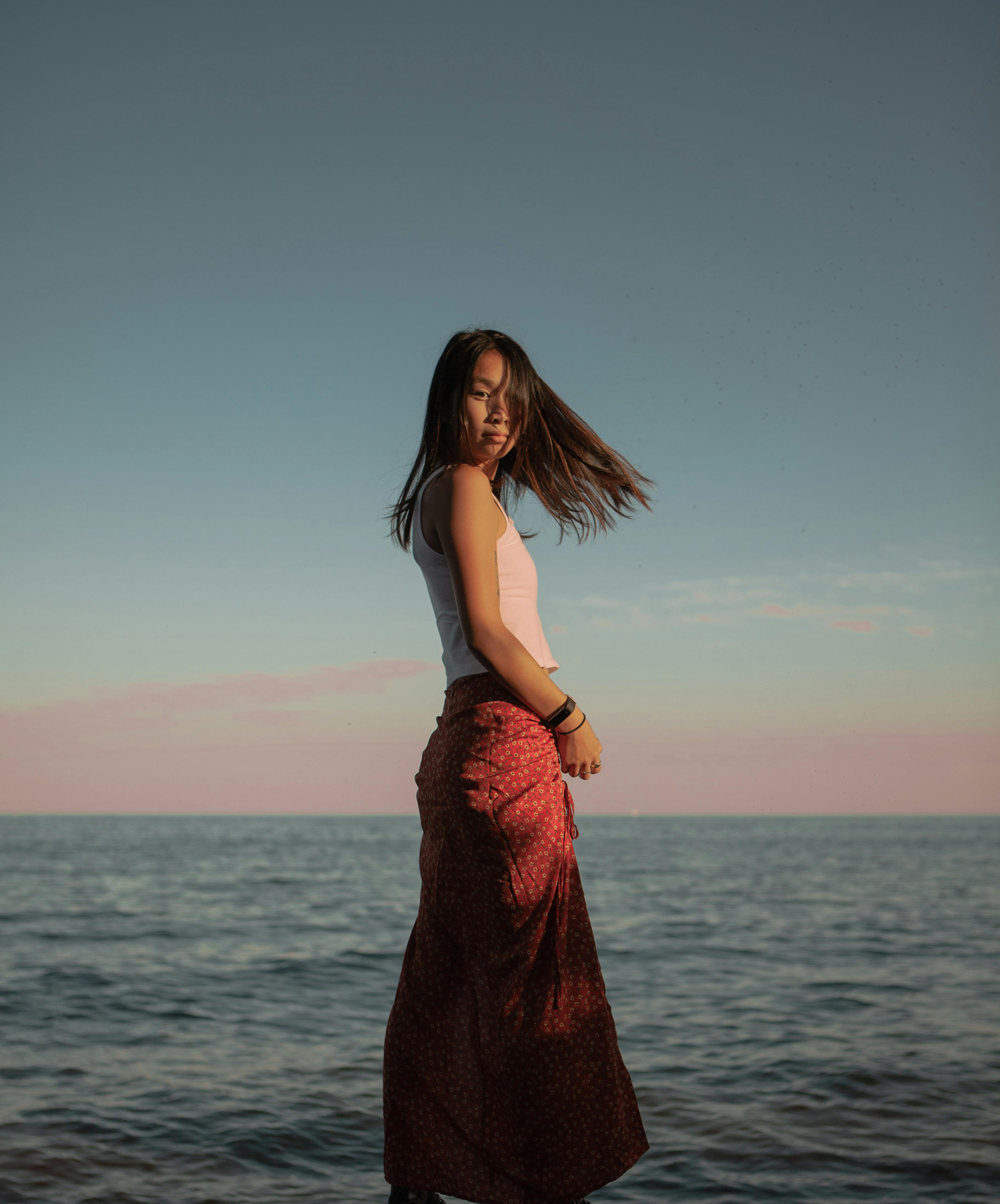 serious ethnic woman standing on sea shore in summer evening