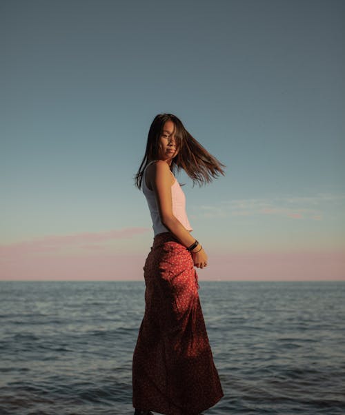 Serious ethnic woman standing on sea shore in summer evening