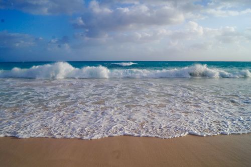Free Peaceful ocean waves gently crashing on a sandy beach under a cloudy sky. Perfect seascape for tranquility and relaxation imagery. Stock Photo