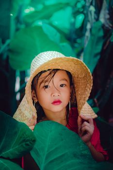 一个戴着草帽的小孩子，置身于户外郁郁葱葱的绿叶之中