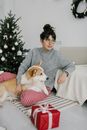 在节日背景下，一名妇女与彭布罗克威尔士柯基坐在圣诞树旁