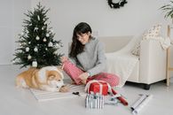 一位女士在圣诞树旁与她的柯基犬一起包装礼物，享受亲密时光