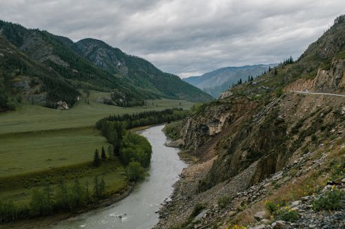 Free Picturesque view of rough mountain slope near stream and green vegetate under cloudy sky Stock Photo