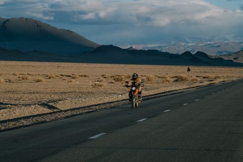 Free Faceless motorcyclist driving on asphalt road near field with plants in mountain valley Stock Photo
