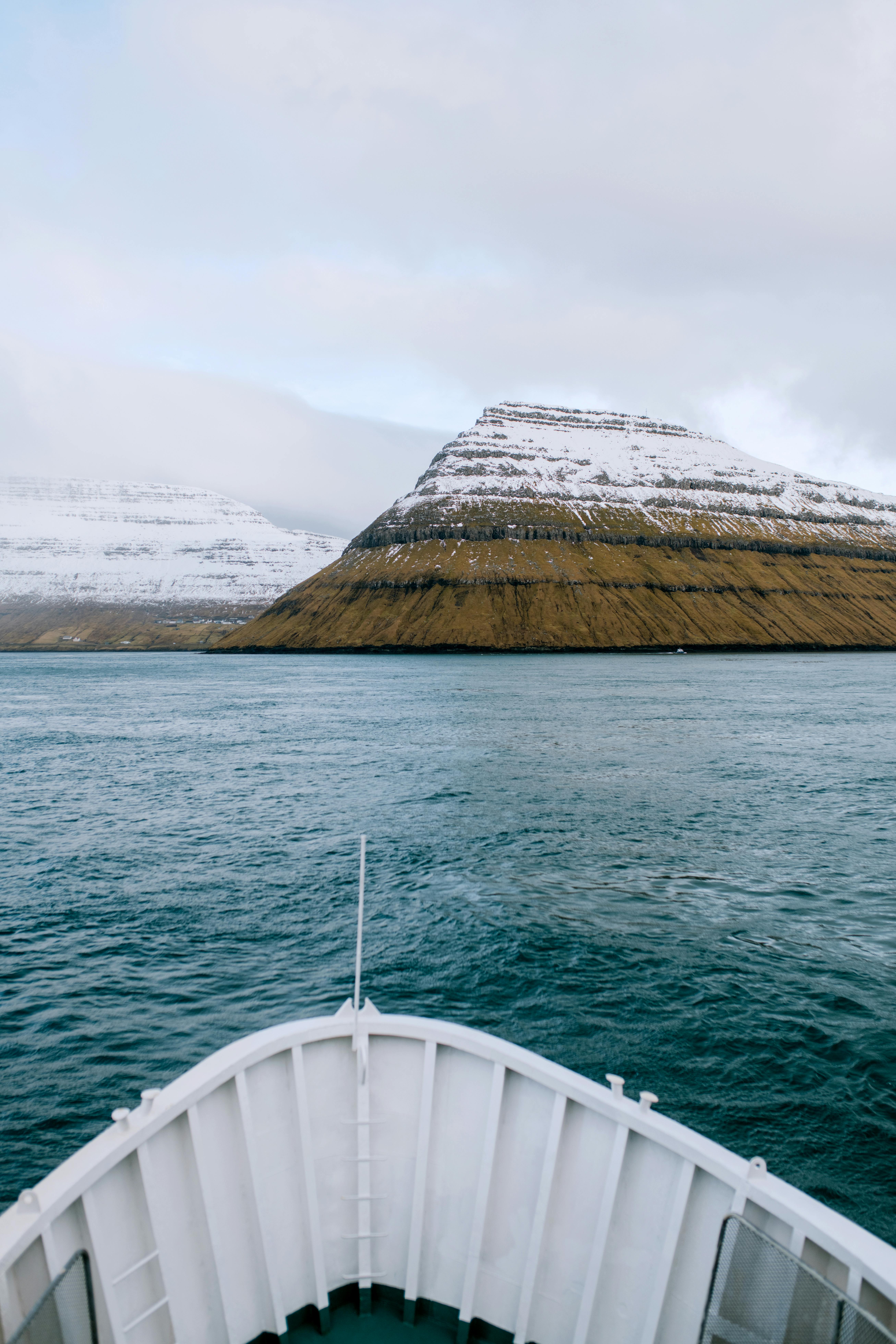法罗群岛宁静的水域中，船头面向白雪皑皑的山脉