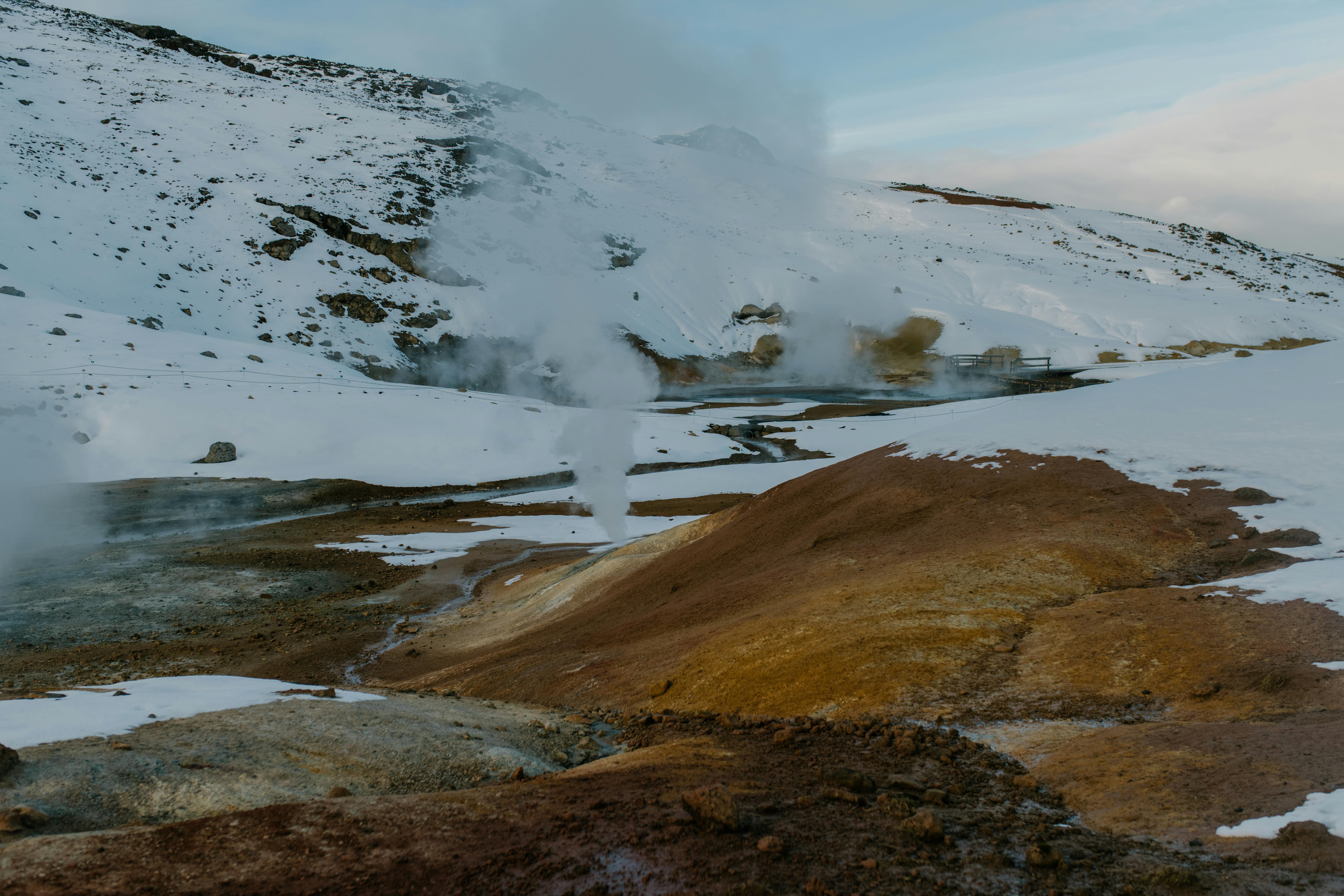 Icelandic geothermal landscape with steam rising from volcanic terrain in a snowy setting.