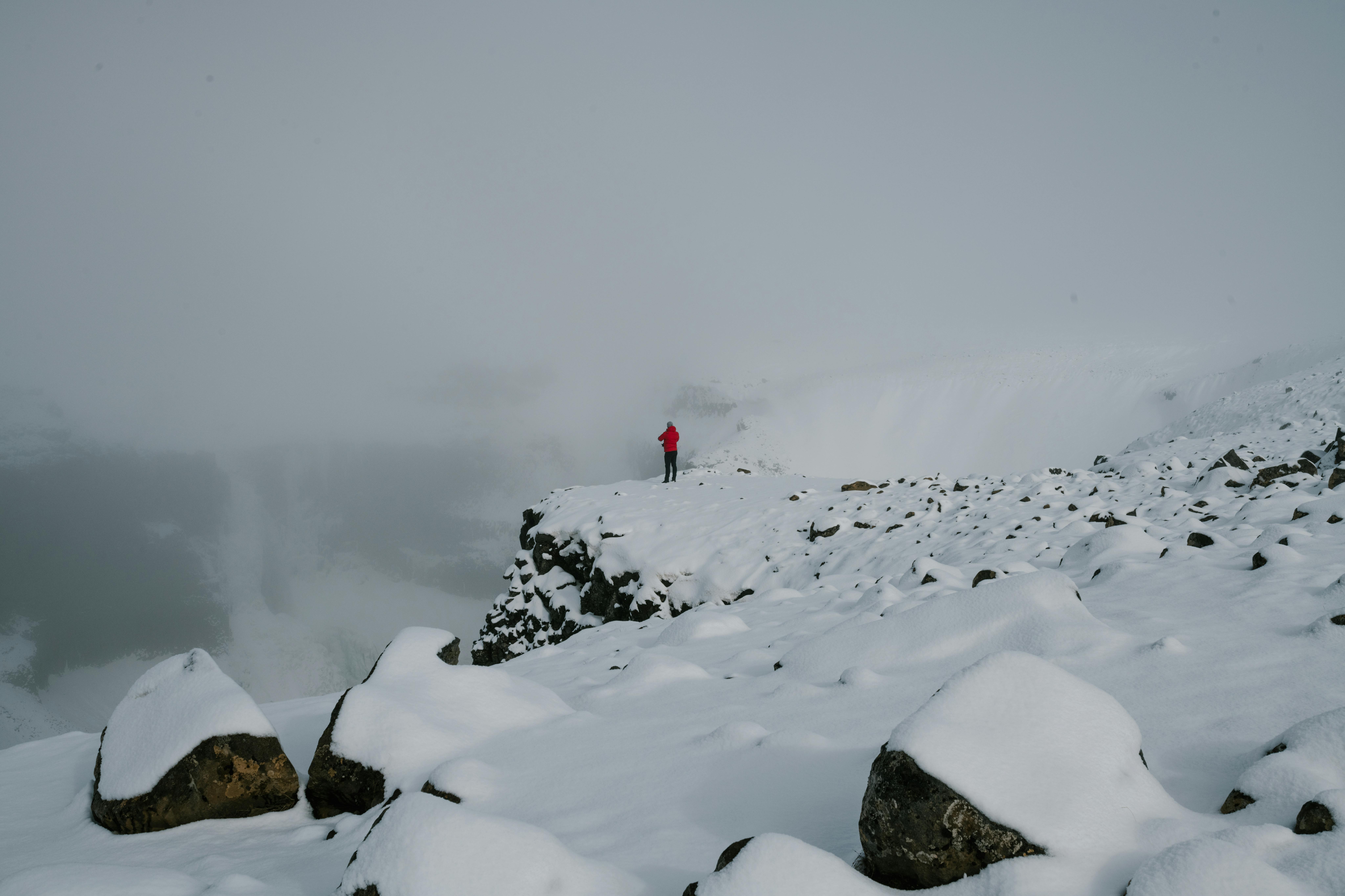 一位孤独的冒险家身着红色夹克，站在冰岛白雪皑皑的悬崖上，四周雾气弥漫