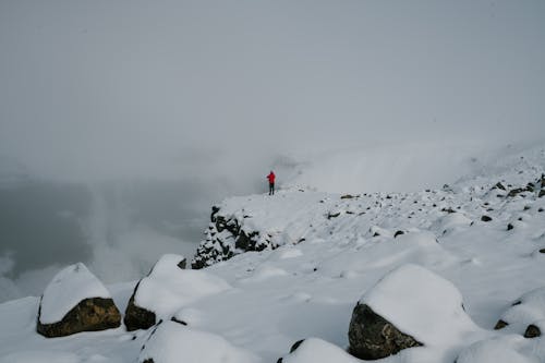 Person In Der Roten Jacke, Die Auf Der Mit Schnee Bedeckten Felsformation Steht