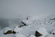 Person in Red Jacket Standing on Rock Formation Covered With Snow