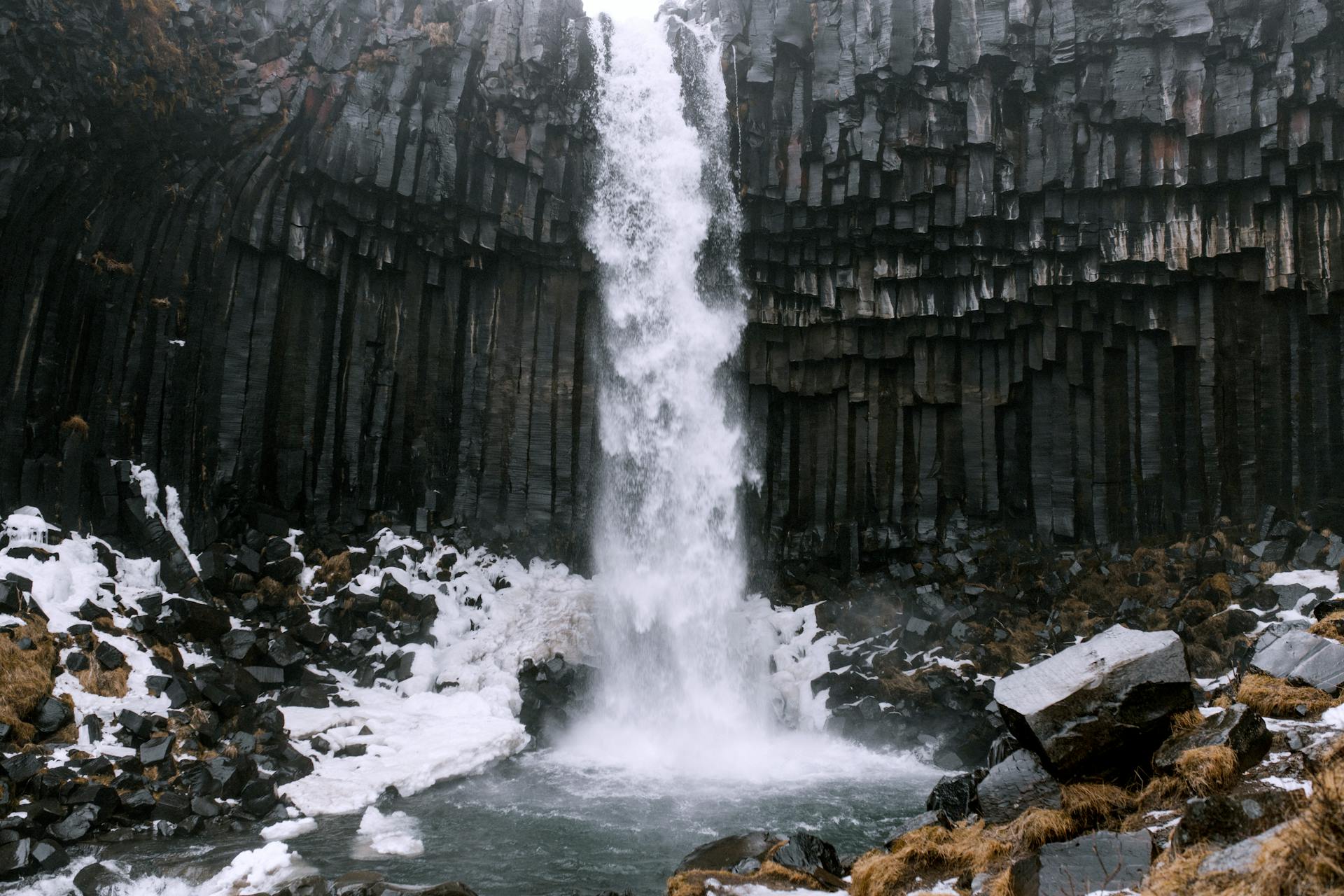 Stunning Icelandic waterfall cascades over unique basalt columns surrounded by snow.