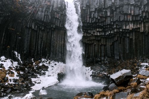 Free Stunning Icelandic waterfall cascades over unique basalt columns surrounded by snow. Stock Photo