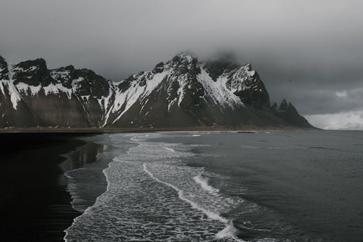 Moody coastal view of Vestrahorn with snow-capped peaks and dark sea in Iceland.