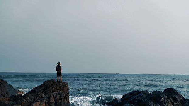 A man gazes at the ocean horizon from rocky cliffs, capturing a tranquil moment by the sea.
