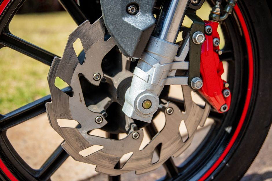 Detailed image of a motorcycle wheel, brake disc, and red caliper in daylight.
