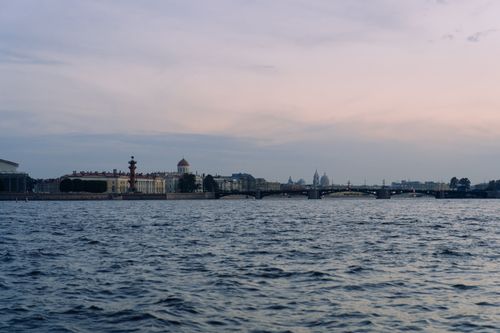 Free A tranquil evening view of a city skyline across a flowing river under a subtle sunset sky. Stock Photo