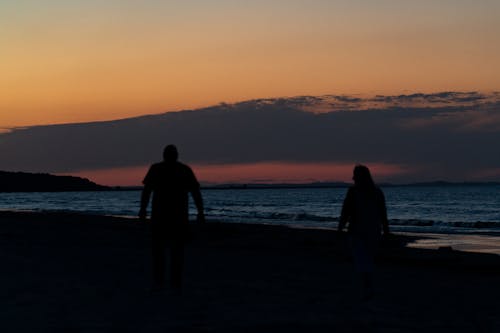 Silhouette of Man and Woman Standing on Beach during Sunset