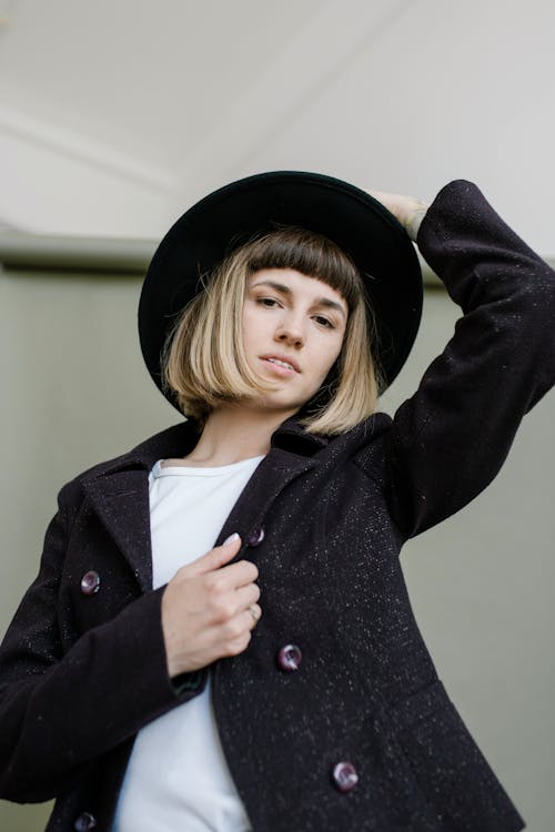 Low angle of young female with modern hairstyle in trendy outfit looking at camera