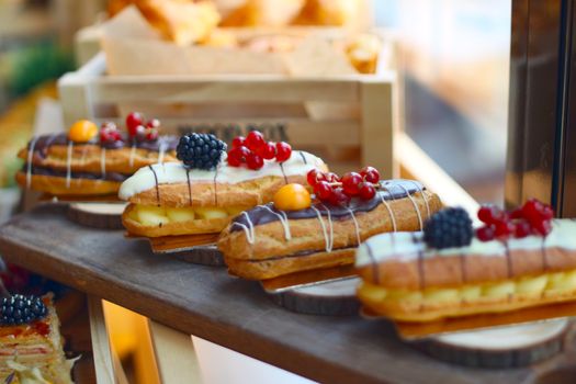 Delicious eclairs topped with fresh berries and cream on a wooden table, perfect for dessert lovers.
