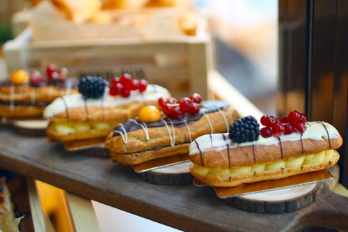 Free Delicious eclairs topped with fresh berries and custard filling on display. Stock Photo