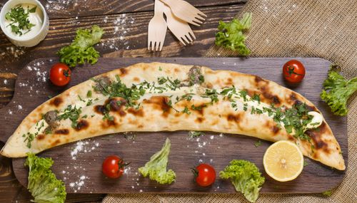 Free Tempting baked pide garnished with fresh herbs, served with cherry tomatoes and lemon on a rustic board. Stock Photo