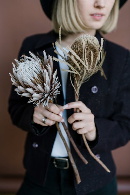 Faceless young female wearing black trousers and jacket standing and showing bouquet of dried flowers