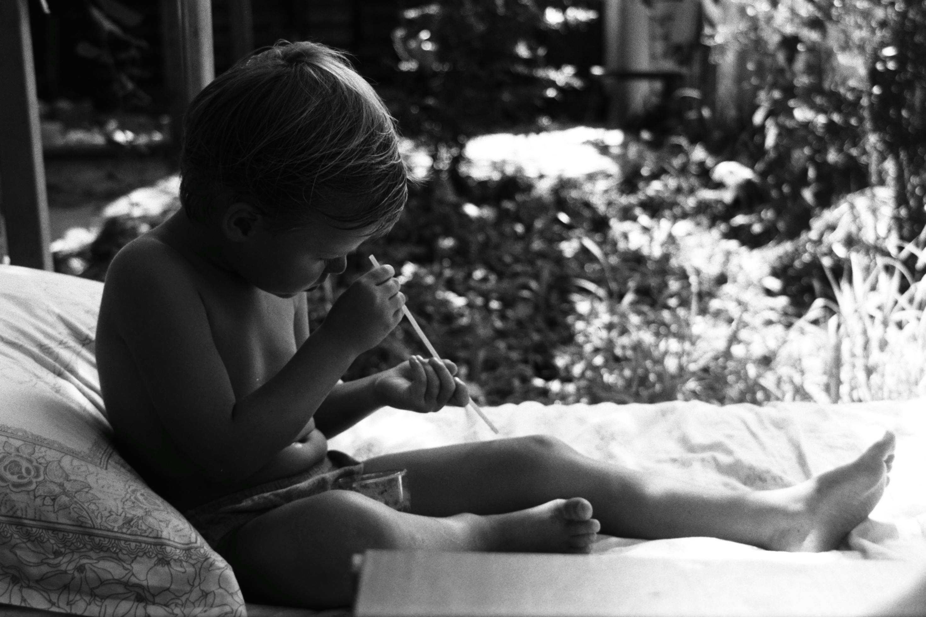 A young child sits outdoors, immersed in playing with a stick, showcasing curiosity and innocence.
