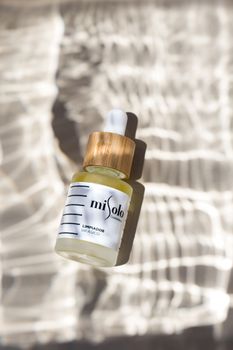 High-angle view of a cosmetic serum bottle casting shadows on a textured surface, showcasing elegance and luxury.
