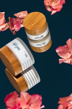 Stylish beauty product photograph featuring wooden jars surrounded by pink petals on a dark background.