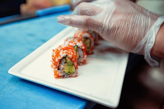 Chef prepares sushi rolls wearing gloves, emphasizing hygiene and precision.