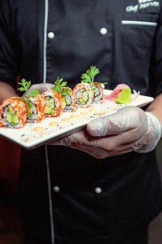 Chef presenting beautifully garnished sushi rolls in a Dubai restaurant setting.