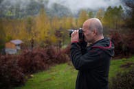 Side view of male photographer standing on grassy hill slope and taking pictures of magnificent landscape