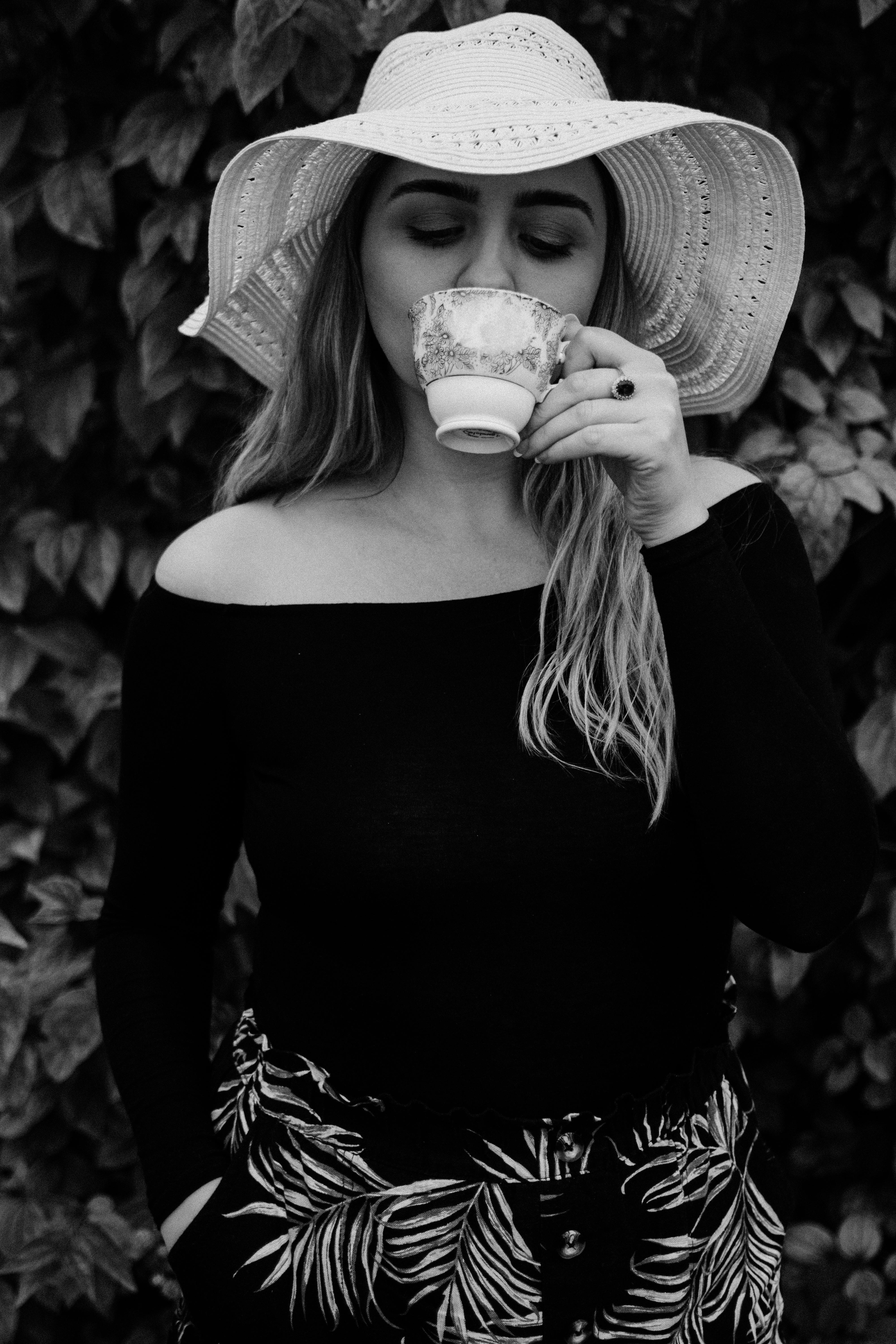 Stylish woman in a hat enjoys a cup of coffee in a leafy garden setting.