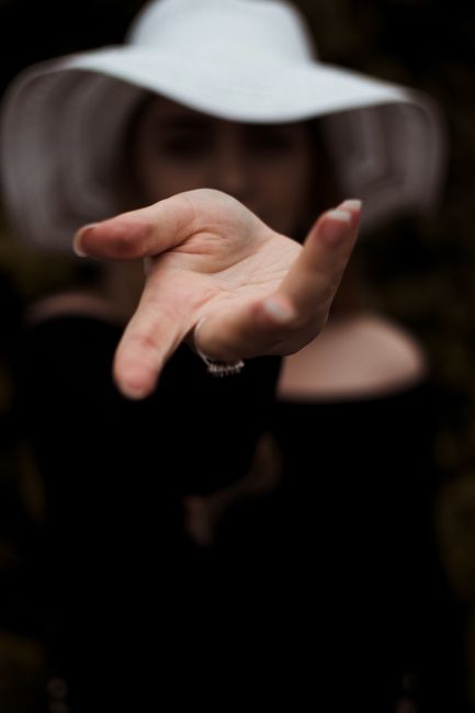 A woman's hand reaching towards the camera, with a white hat and dark background.