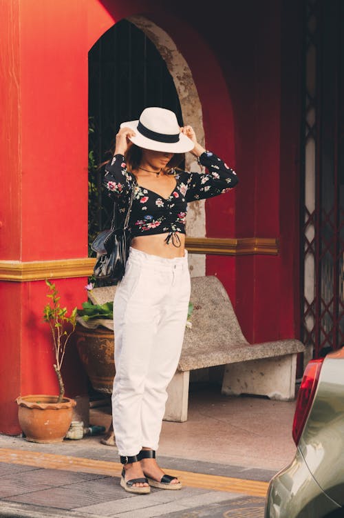 A Woman in Black Crop Top and White Pants Fixing the Hat she is Wearing