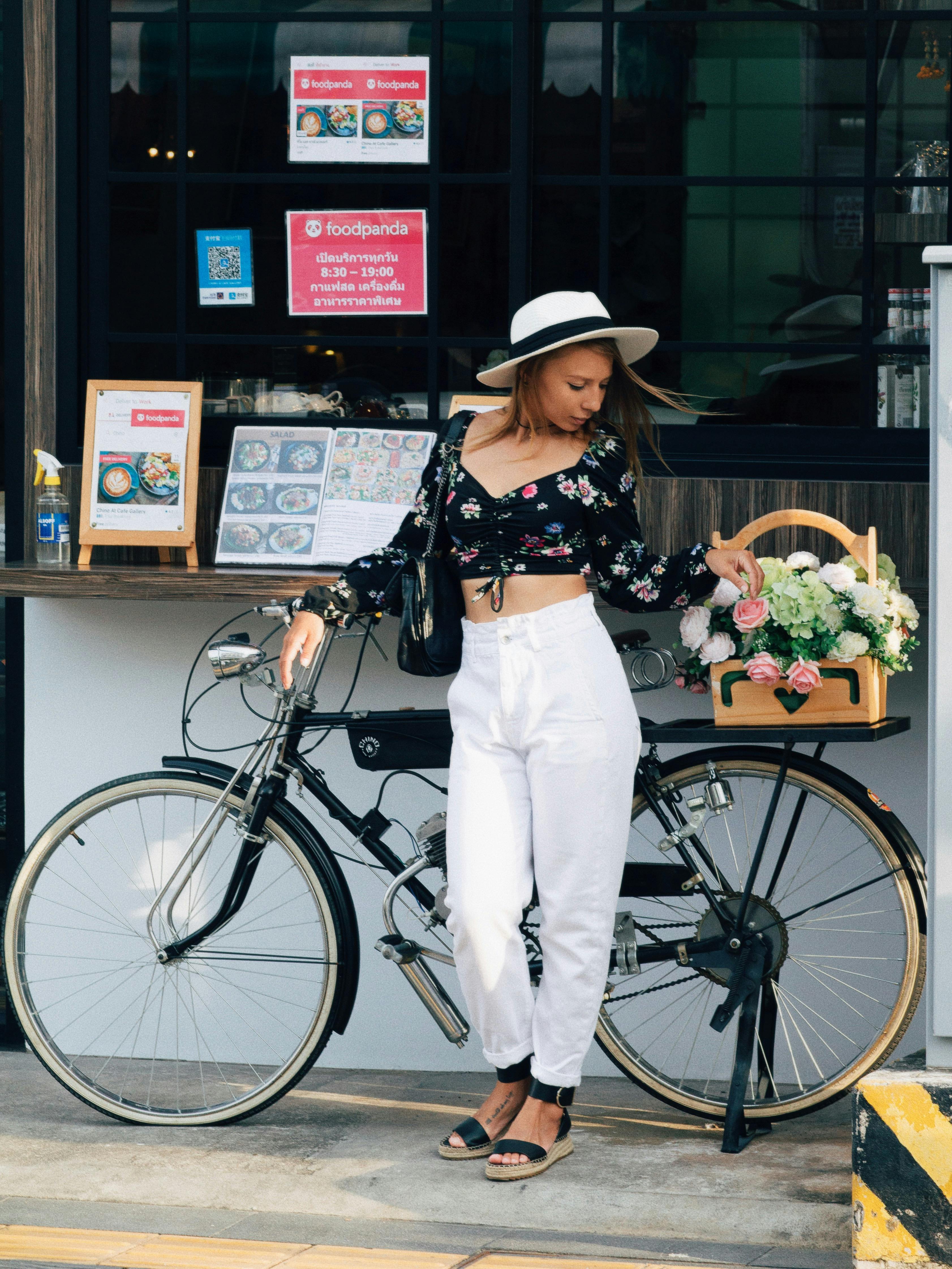 a woman in black floral crop top leaning on a parked bicycle while looking down