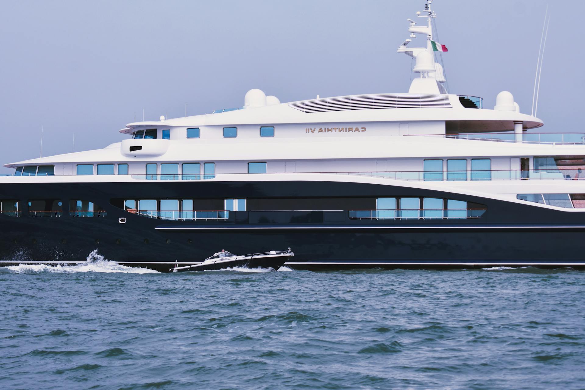 Luxury contemporary private yacht and small motorboat floating in blue ocean against cloudless sky