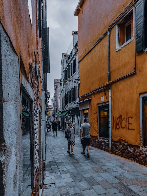 Narrow pedestrian walkway located among old residential buildings in city district under cloudy sky