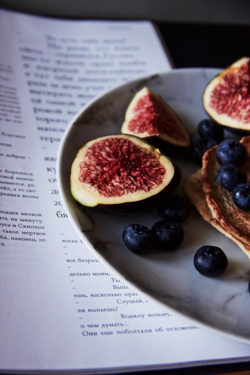 Free Half of plate with tasty sliced figs placed on plate near blueberries and pancakes on table near piece of paper Stock Photo