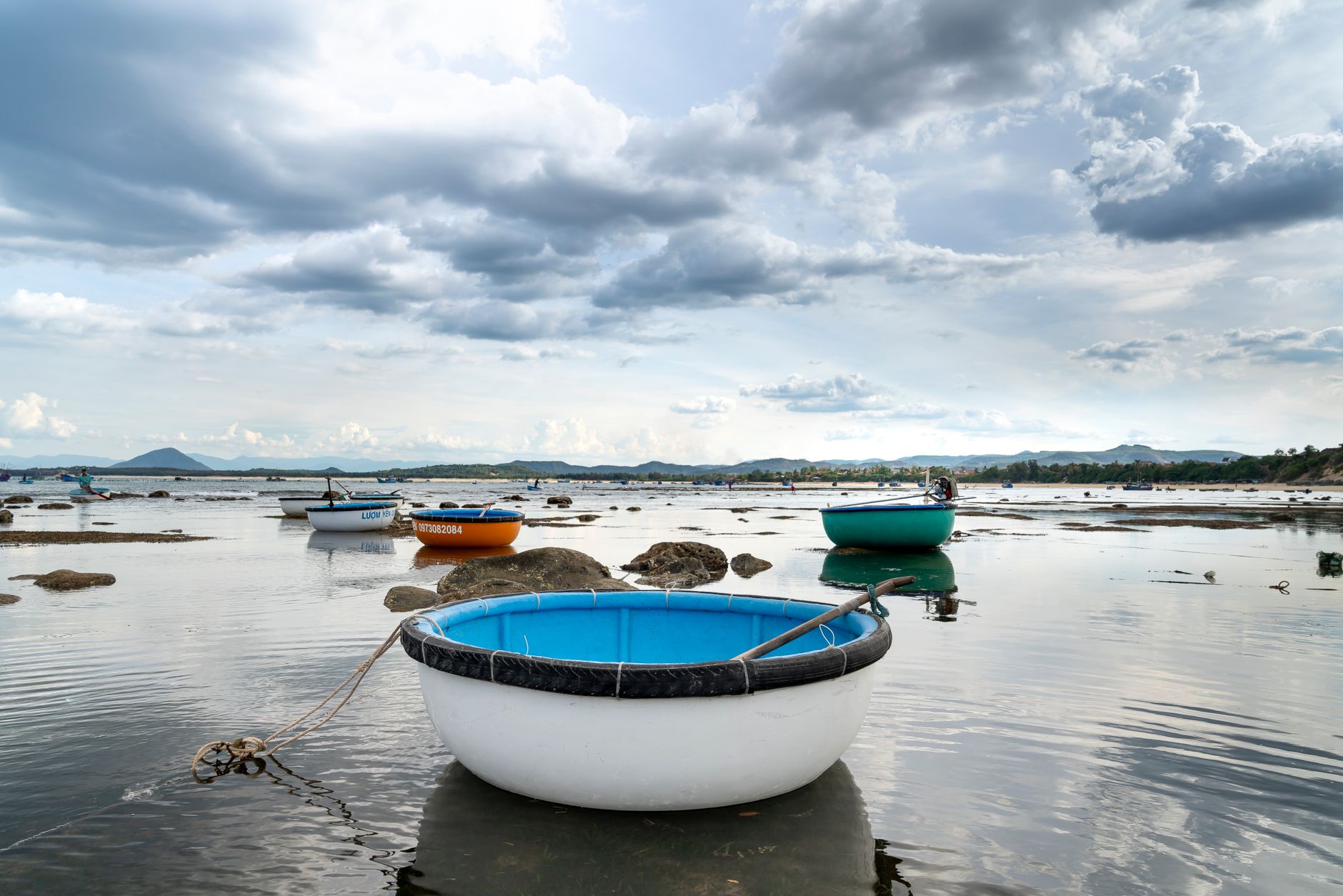 Traditional small Vietnamese round boats moored on rippling shallow water of sea during low tide against cloudy sky