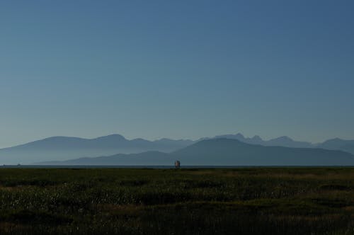 Silhouette of Mountains From the Green Grass Field Under Blue Sky