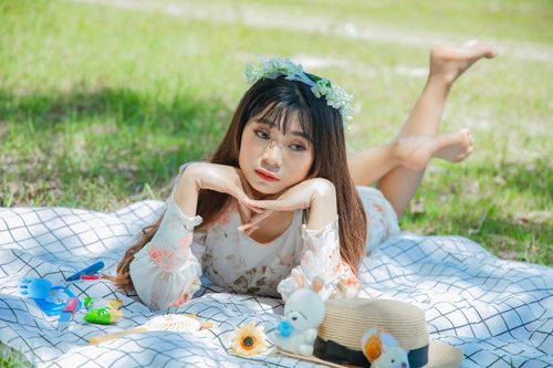 Free Young woman in floral dress with flower crown relaxing on a picnic blanket outdoors. Stock Photo