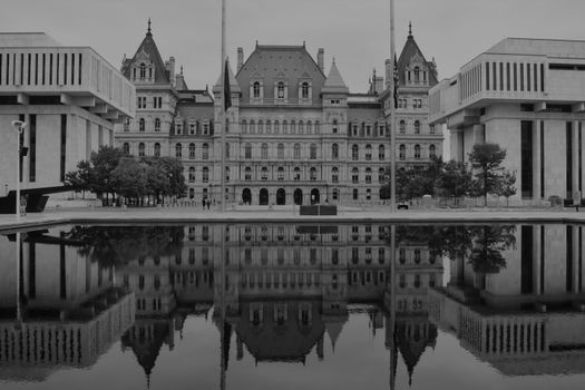 Monochrome photo of the New York State Capitol building with its reflection in water, emphasizing architectural symmetry.