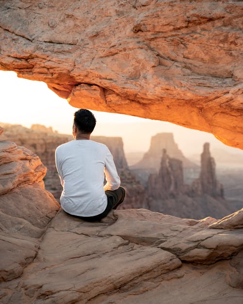 Free Man in White Shirt Sitting on Brown Rock Formation Stock Photo