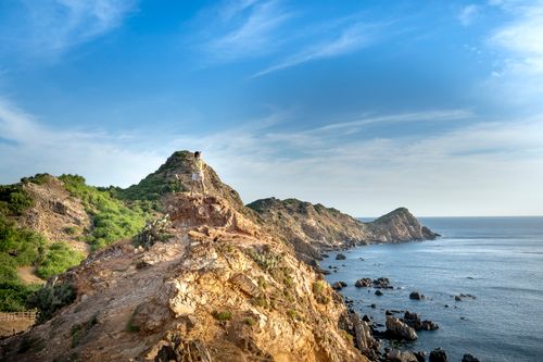 Free Full length unrecognizable person in summer wear standing with hands on waist on rocky cliff and admiring blue peaceful sea Stock Photo