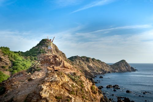 Free Full body faceless person standing with arms raised in excitement on rough cliff on seashore beneath clear blue sky Stock Photo