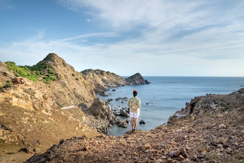 Faceless person standing on rocky bay shore