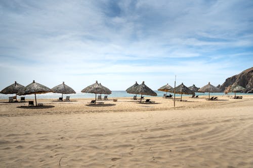 Spacious sandy beach with straw umbrellas and sunbeds near azure seawater beneath clear blue sky on hot summer day